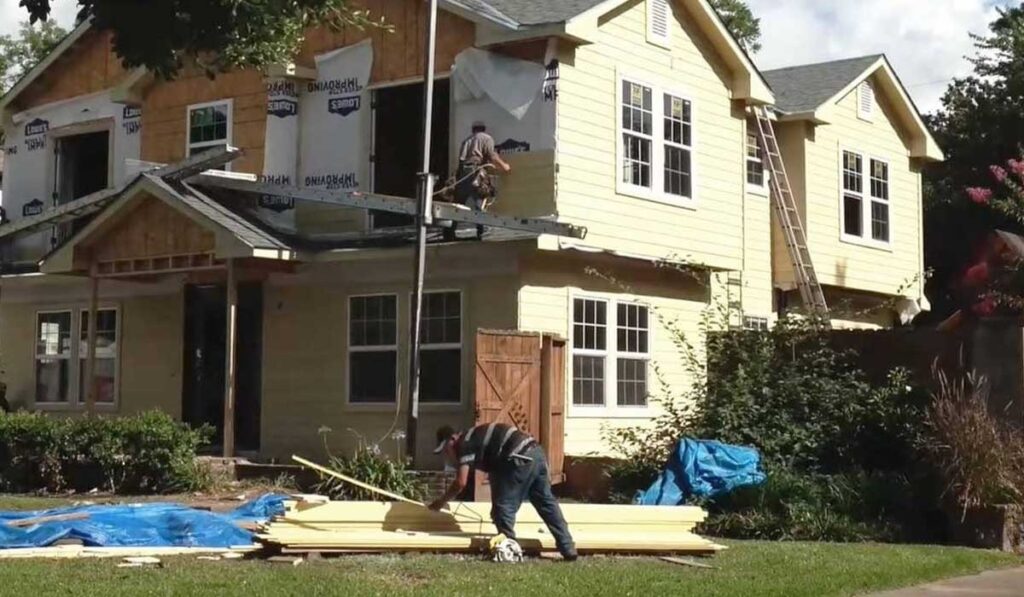 Workers are installing siding on a large two-story home addition during a remodeling project.