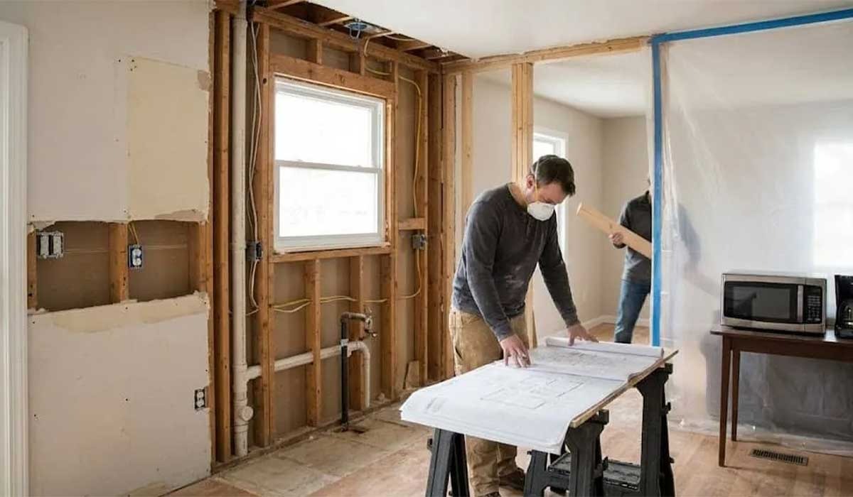 Contractor reviews plans during rough-in phase with a temporary kitchen visible behind a dust barrier.