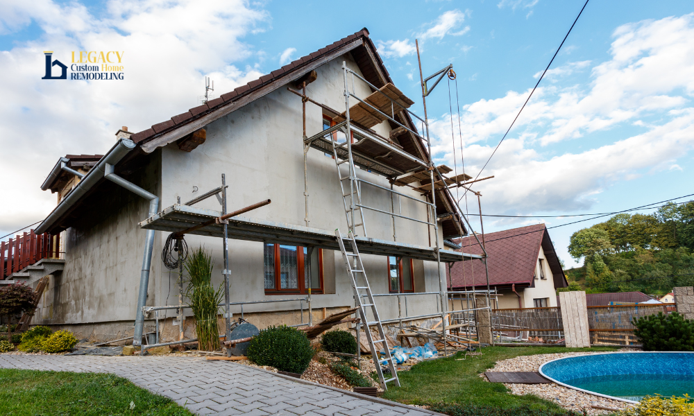 The image shows a house under renovation with scaffolding on the side, set against a partly cloudy sky. A small round pool and landscaped garden can be seen in the foreground, creating a sense of transformation and progress.
